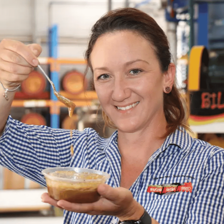 Sarina Sugar Shed staff member in branded uniform lifting a spoon of golden syrup from a tasting cup on the working sugar mill floor