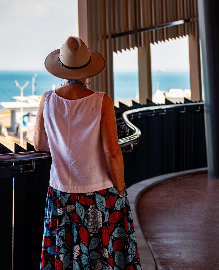 Visitor in a wide-brimmed hat looks out over Darwin Harbour from a curved walkway at the Larrakia Cultural Centre, NT