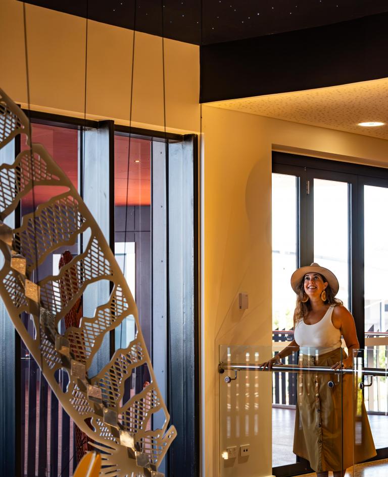 Visitor in a wide-brimmed hat looks up at a patterned metal sculpture inside the Larrakia Cultural Centre, Darwin NT